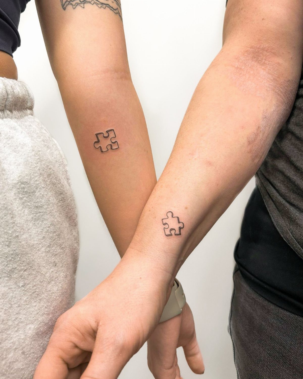 Two forearms with matching small black puzzle piece tattoos on the inner wrists.