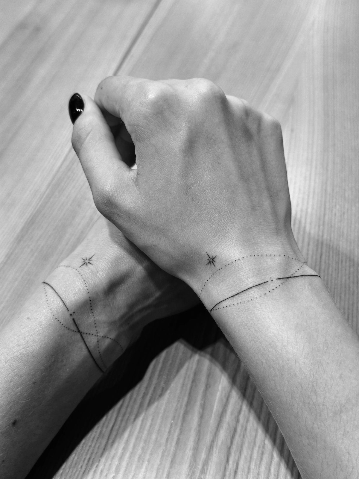 Two wrists with matching star and curved line tattoos on a wooden background