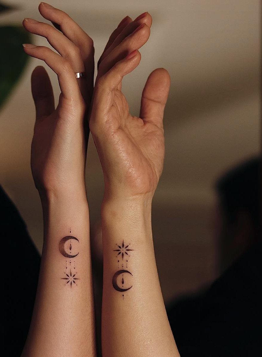 Two wrists with matching tattoos of a crescent moon and a small star.