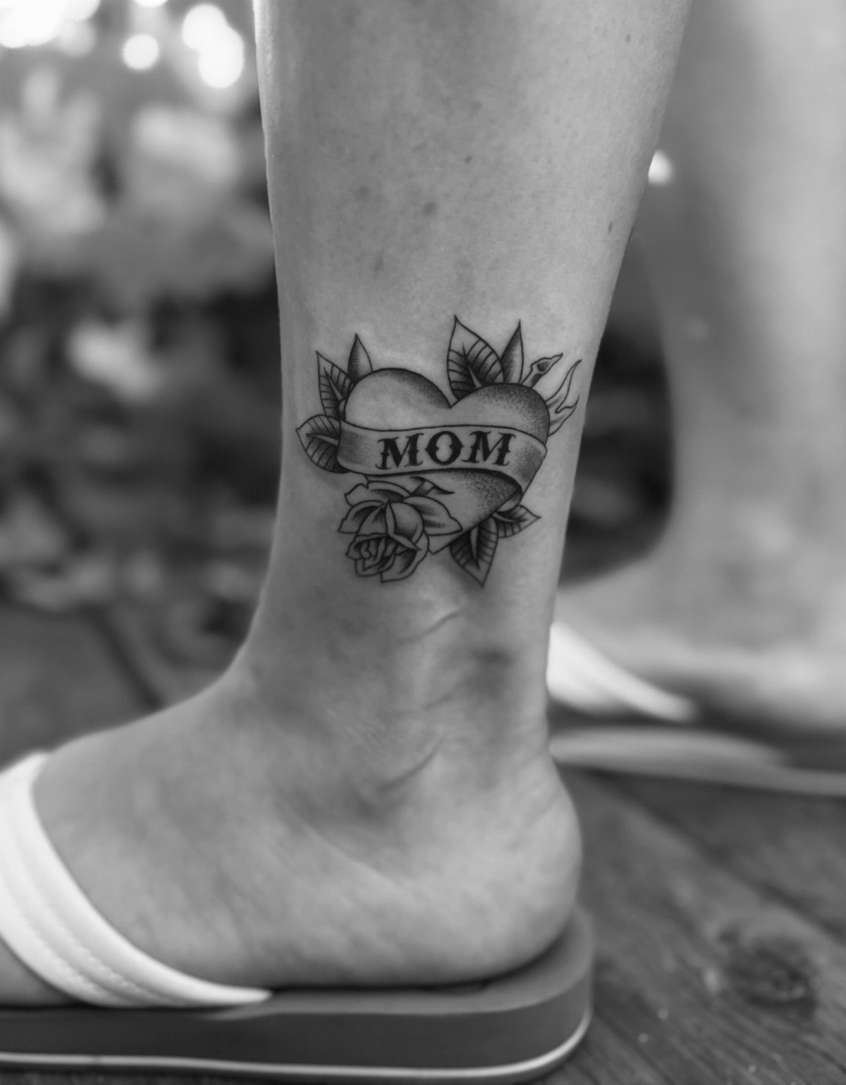 Heart tattoo with MOM banner and rose on a person's ankle.