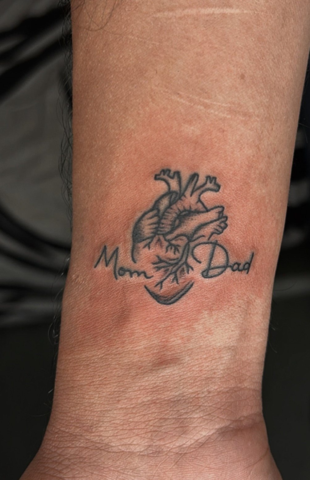 Anatomical heart tattoo on a wrist with the words Mom and Dad.