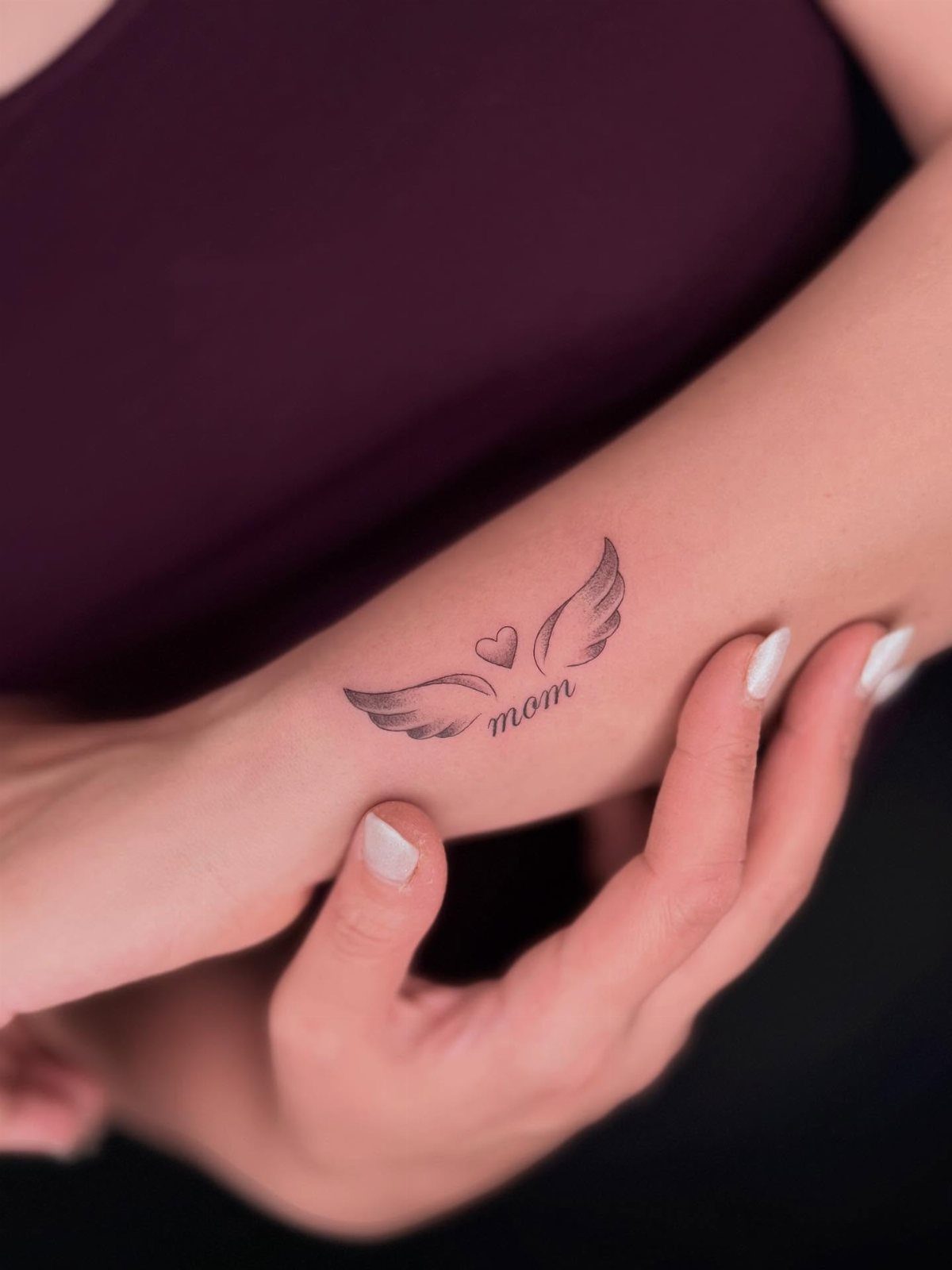 Heart and wings tattoo with the word mom on a person's wrist