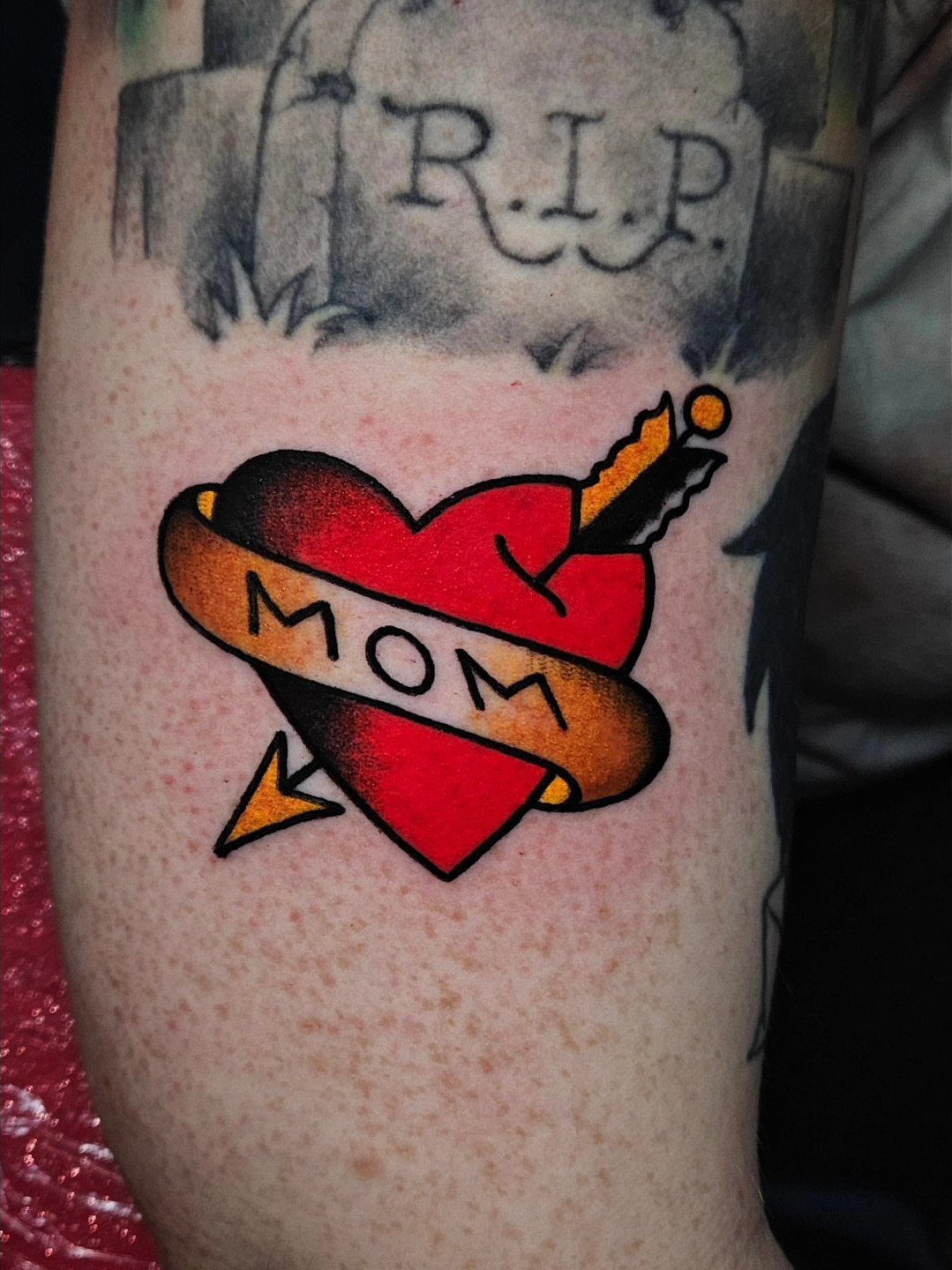 Red heart tattoo with MOM banner and arrow on a person's arm