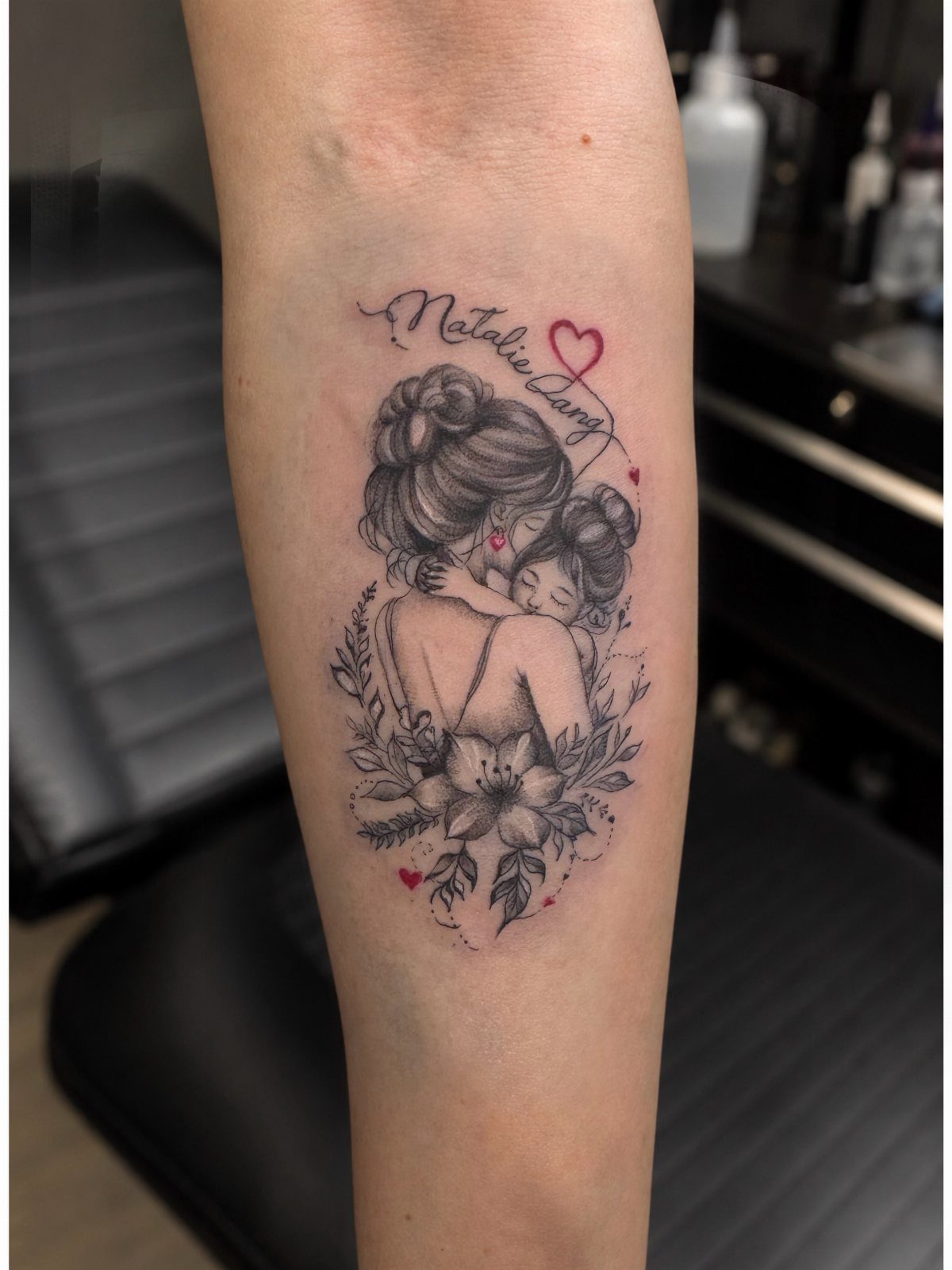 Black and grey tattoo of a mother hugging a child with red hearts