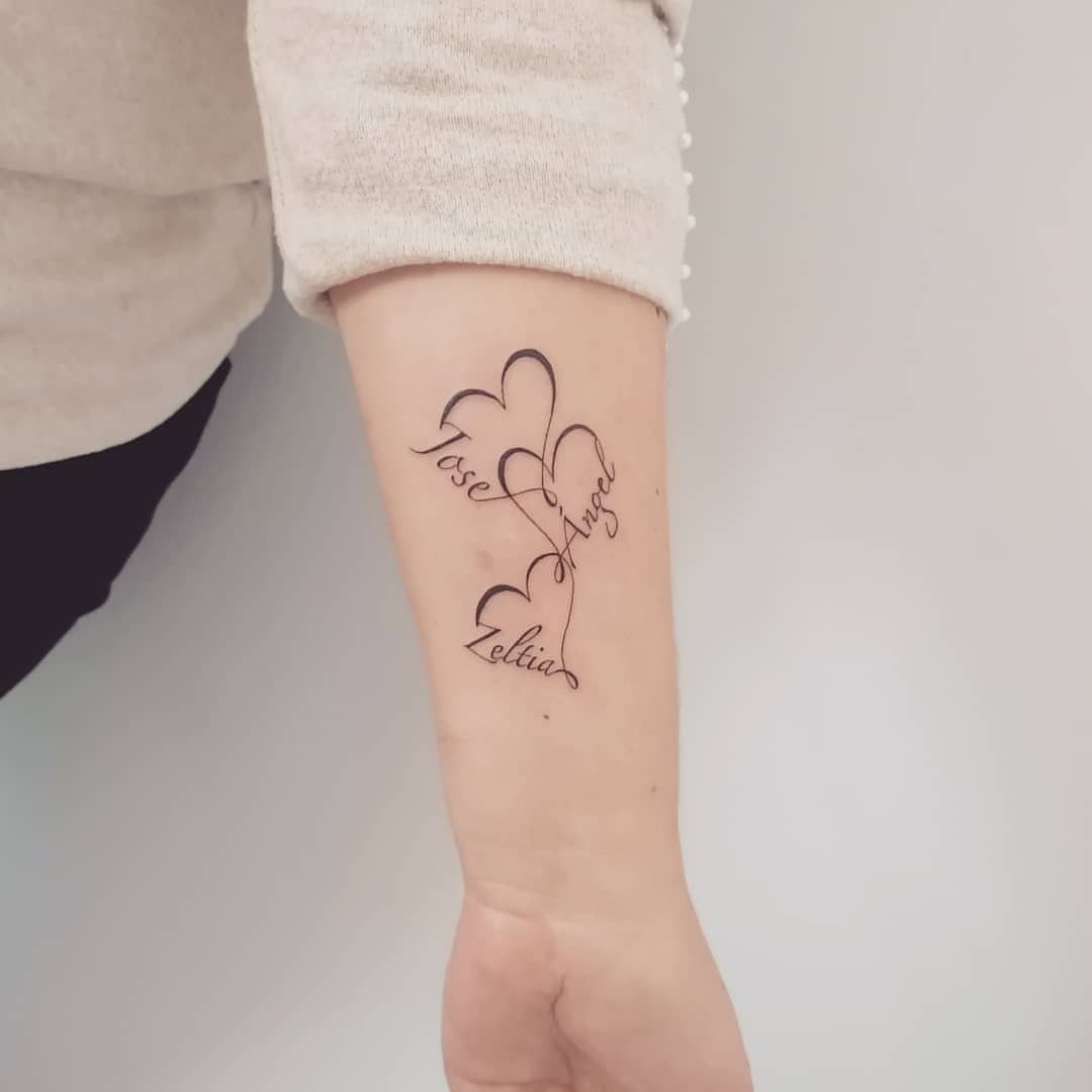 Three cursive name tattoos integrated into heart outlines on a person's inner forearm.
