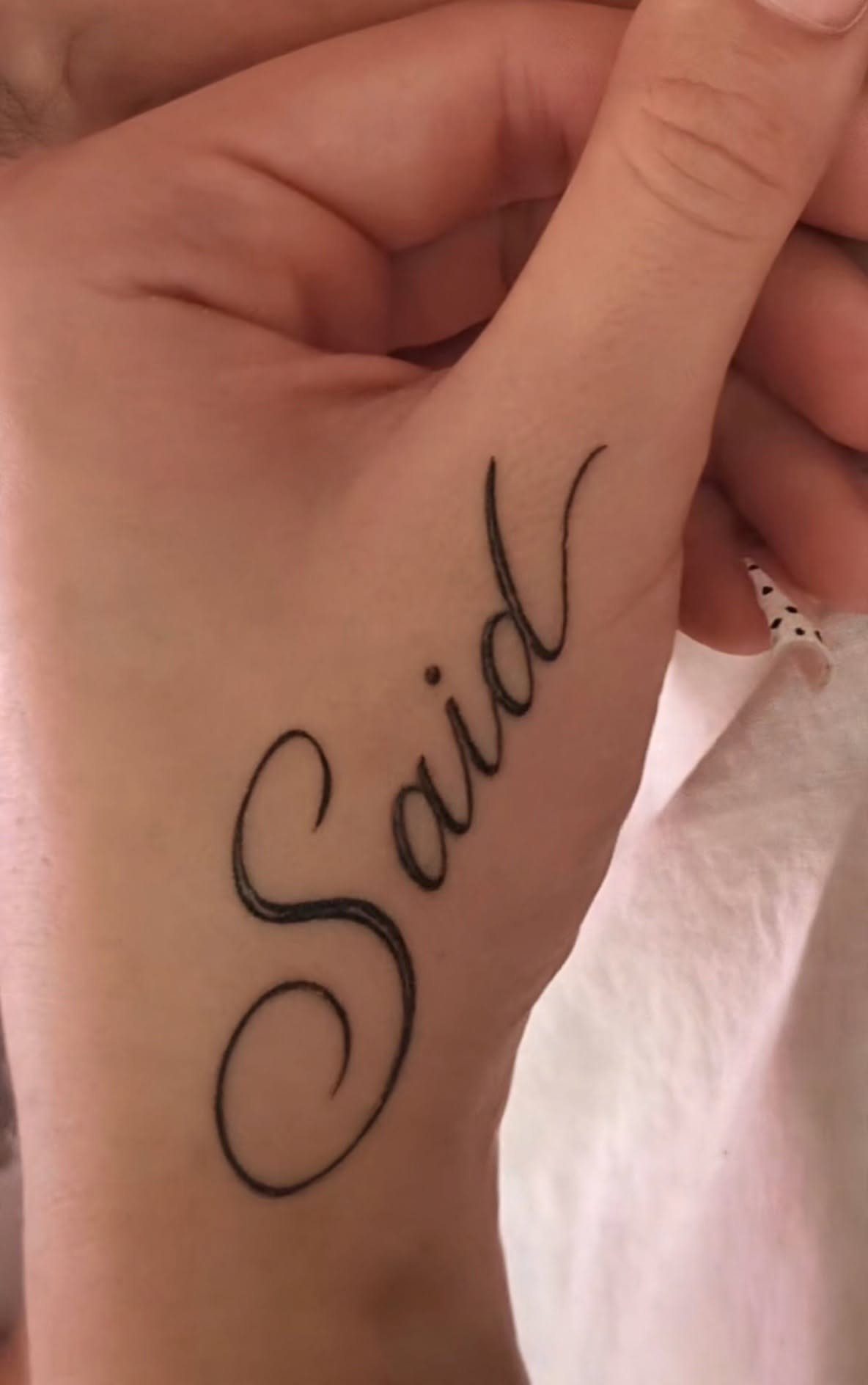 Cursive name tattoo reading Said placed vertically on the side of a hand