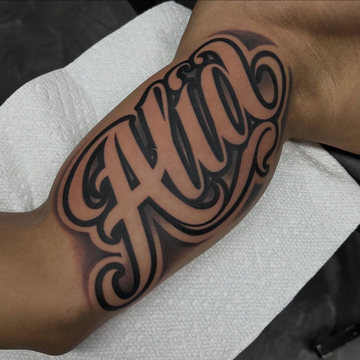 Bold black ink name tattoo of Alia on a person's forearm