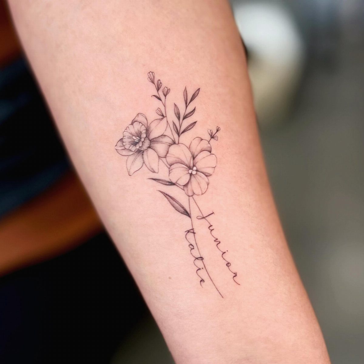 Floral tattoo on a forearm with the names Junior and Katie in script