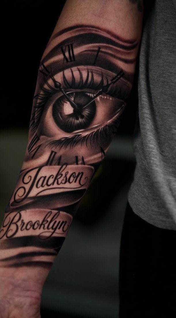Realism tattoo on forearm featuring a detailed eye, clock face, and names Jackson and Brooklyn.