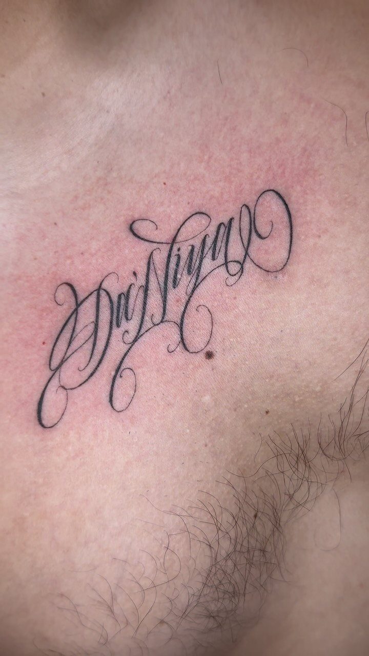 Cursive script name tattoo with decorative flourishes on a person's chest