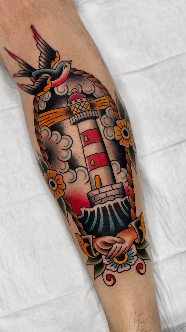 Traditional style tattoo of a lighthouse with a swallow and flowers on forearm