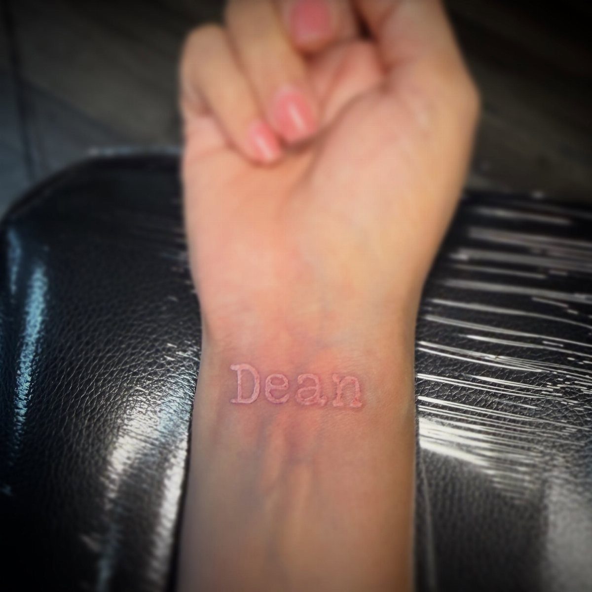 White ink tattoo of the name Dean on a person's inner wrist