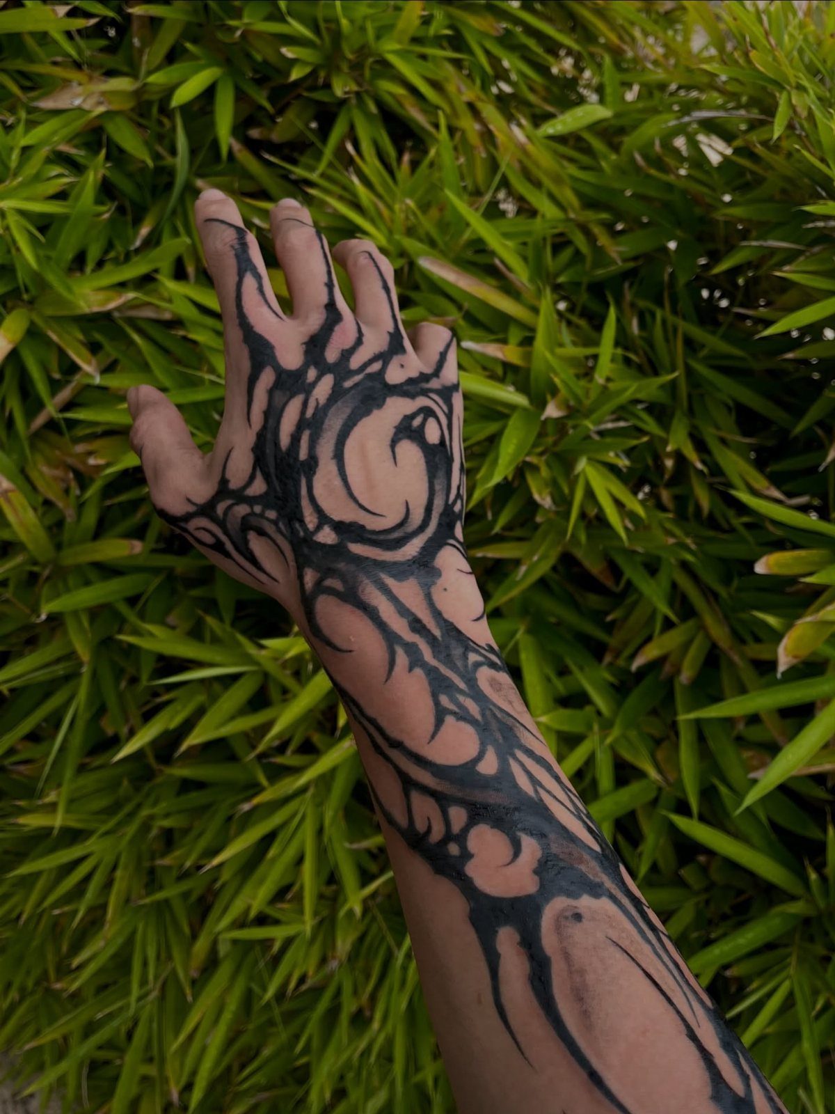 Hand and forearm with a black neo-tribal tattoo against green leaves