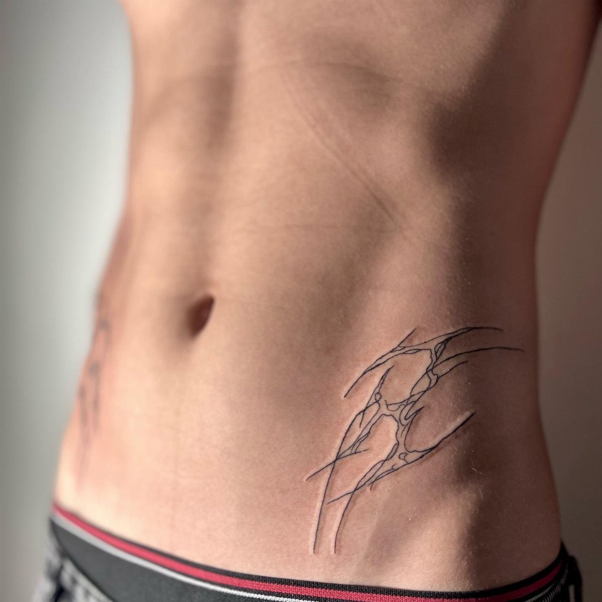 Neo-tribal tattoo with sharp black abstract lines on a person's lower abdomen and hip.