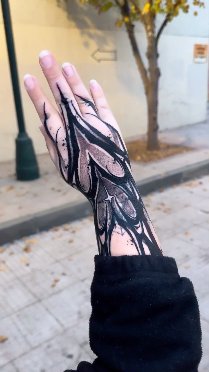 Hand and wrist with a bold black neo-tribal tattoo in an outdoor setting.