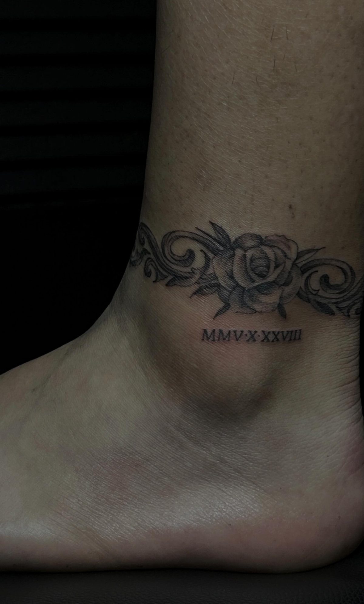 Ankle tattoo featuring a decorative rose band and Roman numeral date below it.