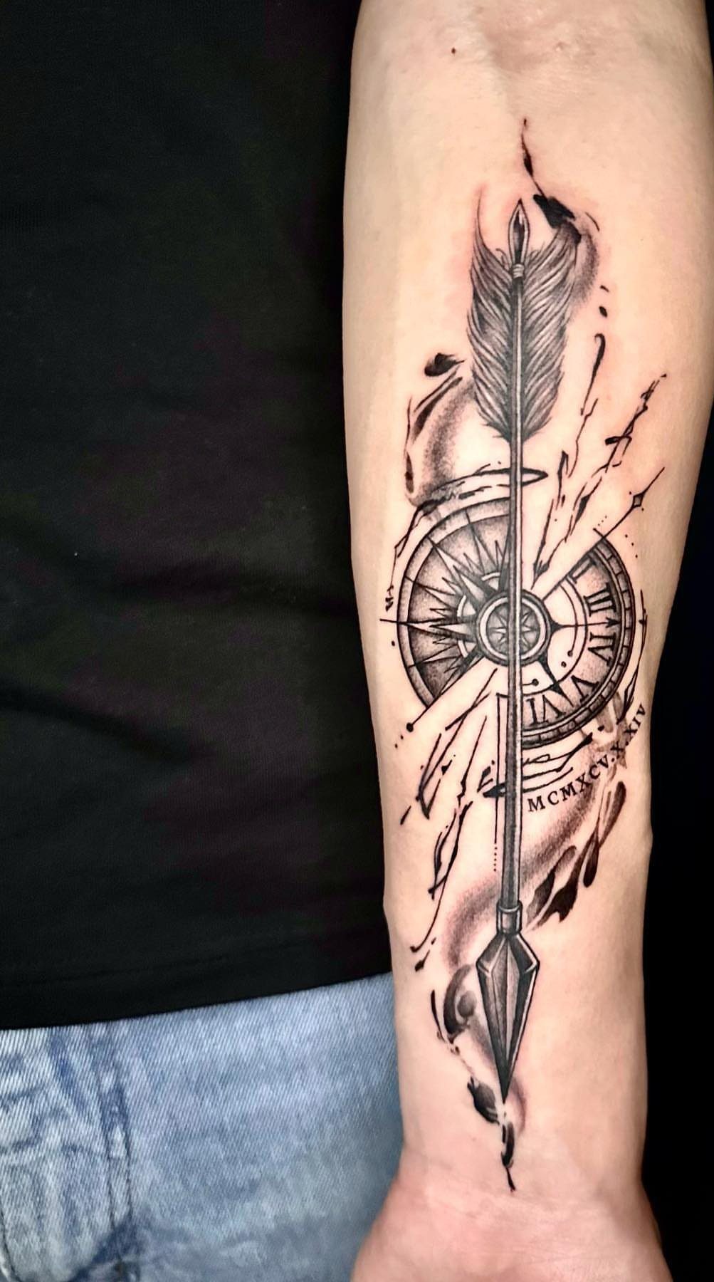 Arrow tattoo with roman numeral compass on a person's forearm in black ink