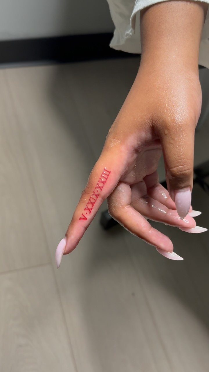 Red Roman numeral tattoo on the side of a person's index finger