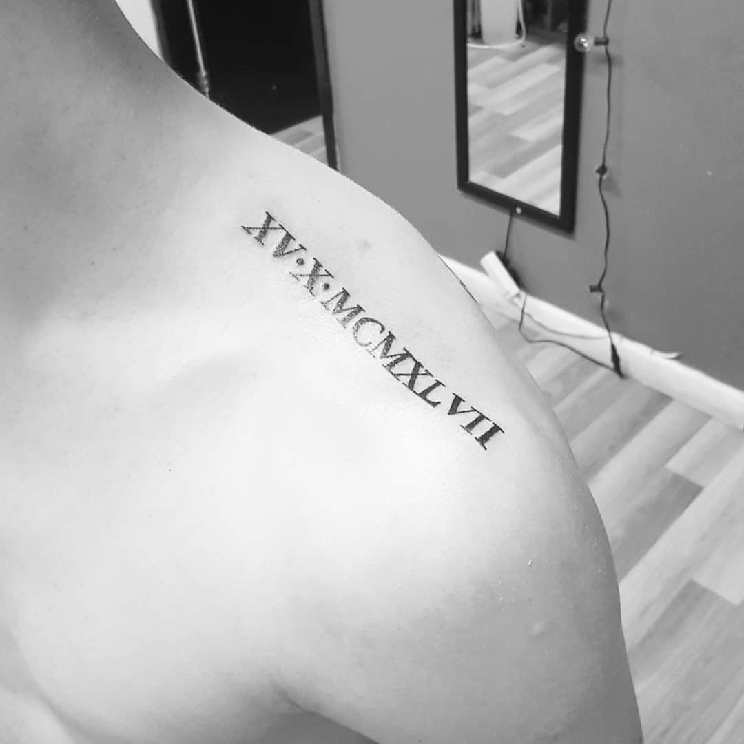 Roman numeral tattoo on the top of a person's shoulder and upper back.