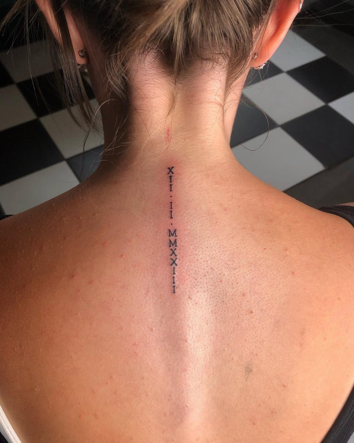 Roman numeral tattoo aligned vertically down the center of a person's upper spine.