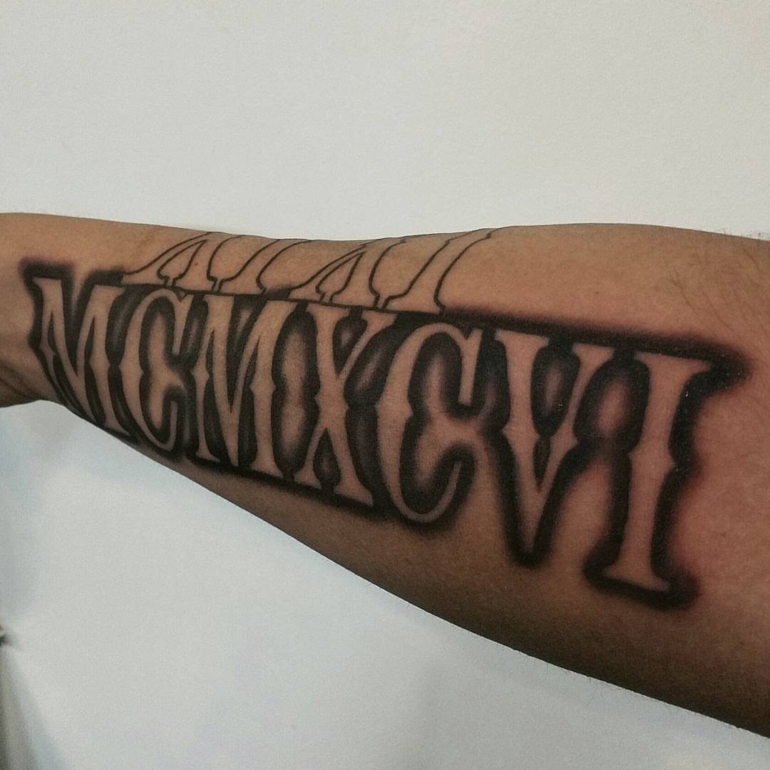 Bold Roman numeral tattoo MCMXCVI in gothic style on a person's upper arm.