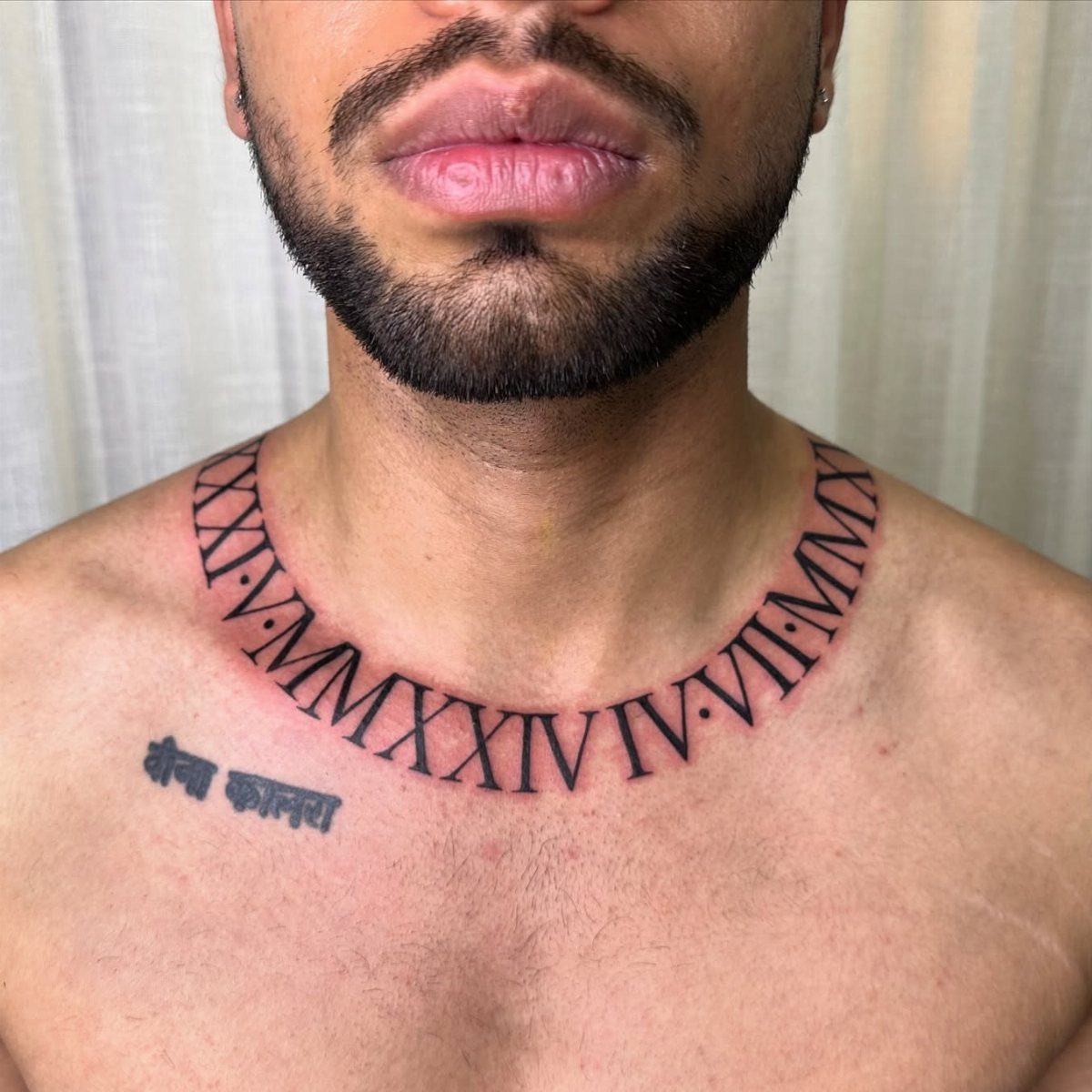 Curved Roman numeral tattoo wrapping around a man's neck and collarbone area.