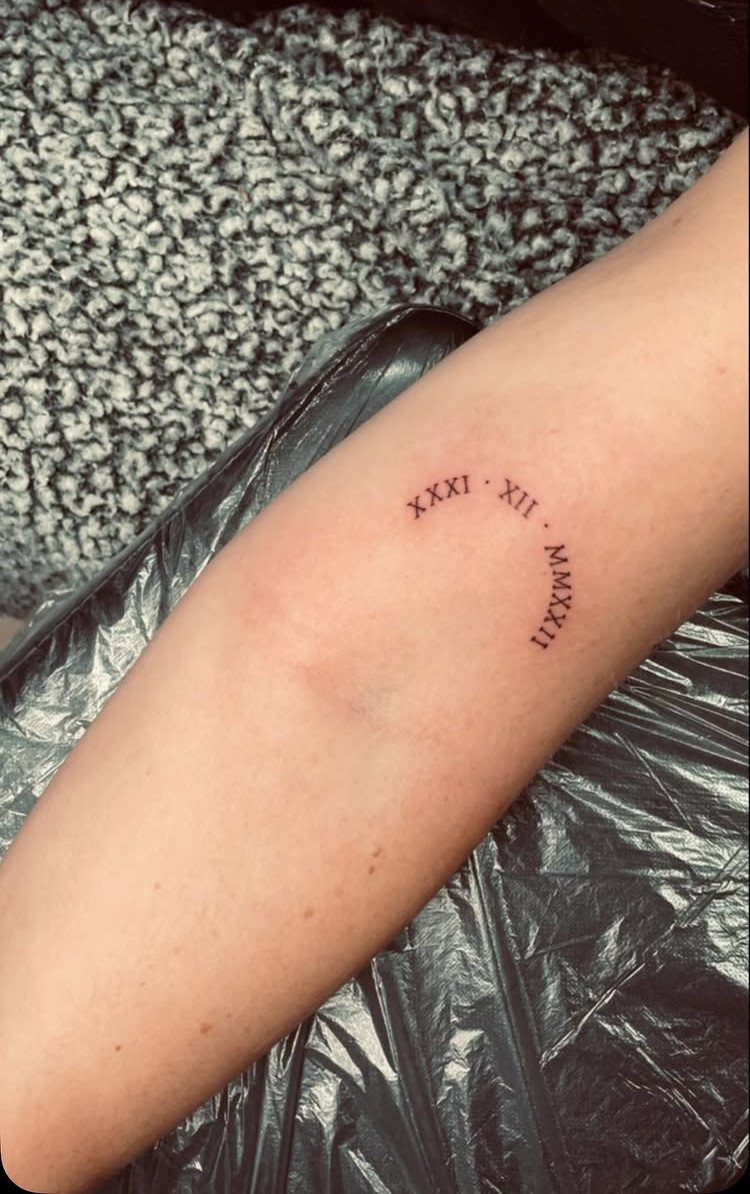 Curved Roman numeral date tattoo on a person's fair-skinned forearm.