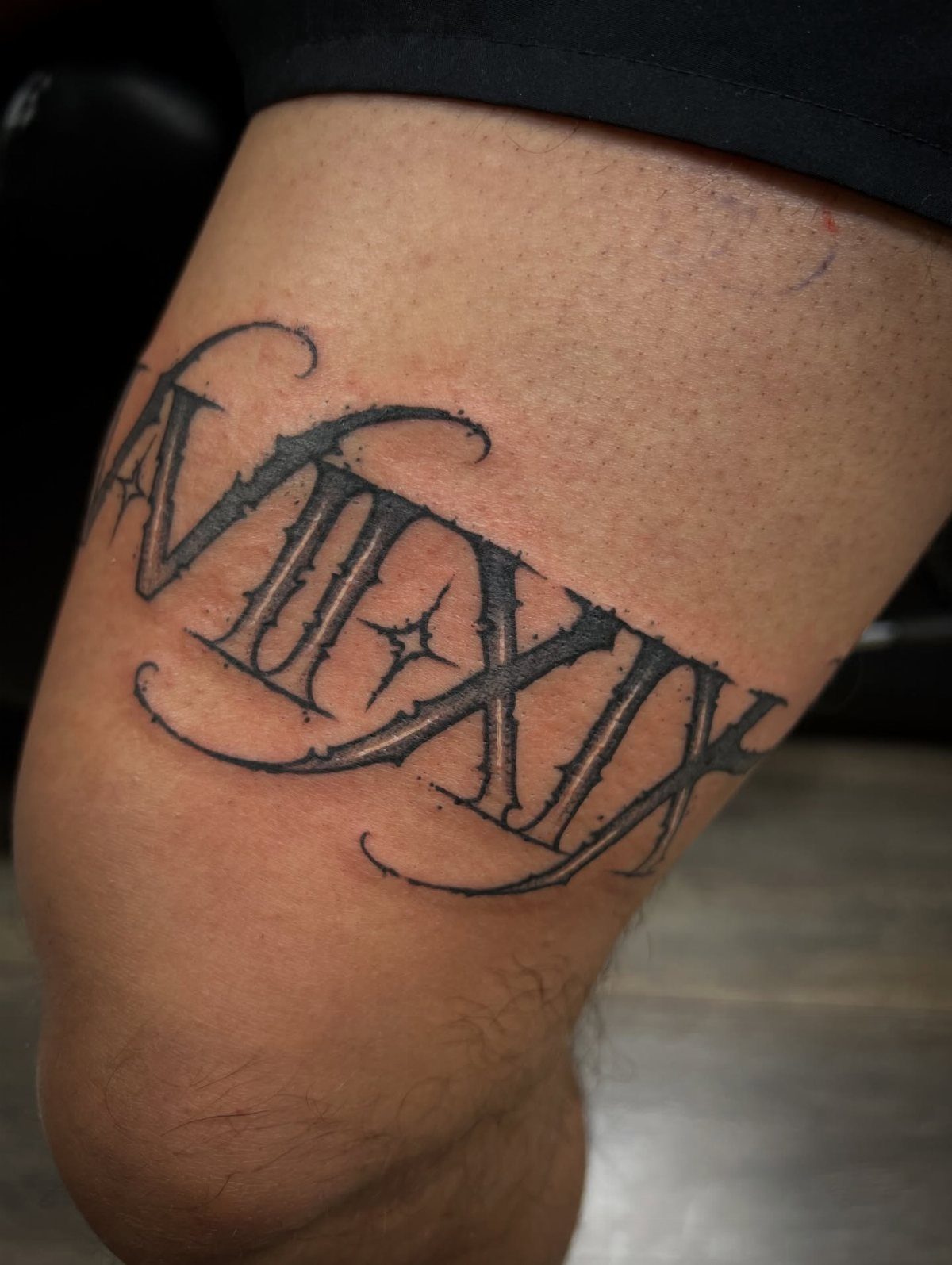 Roman numeral tattoo with decorative swirls and a star on a person's leg.