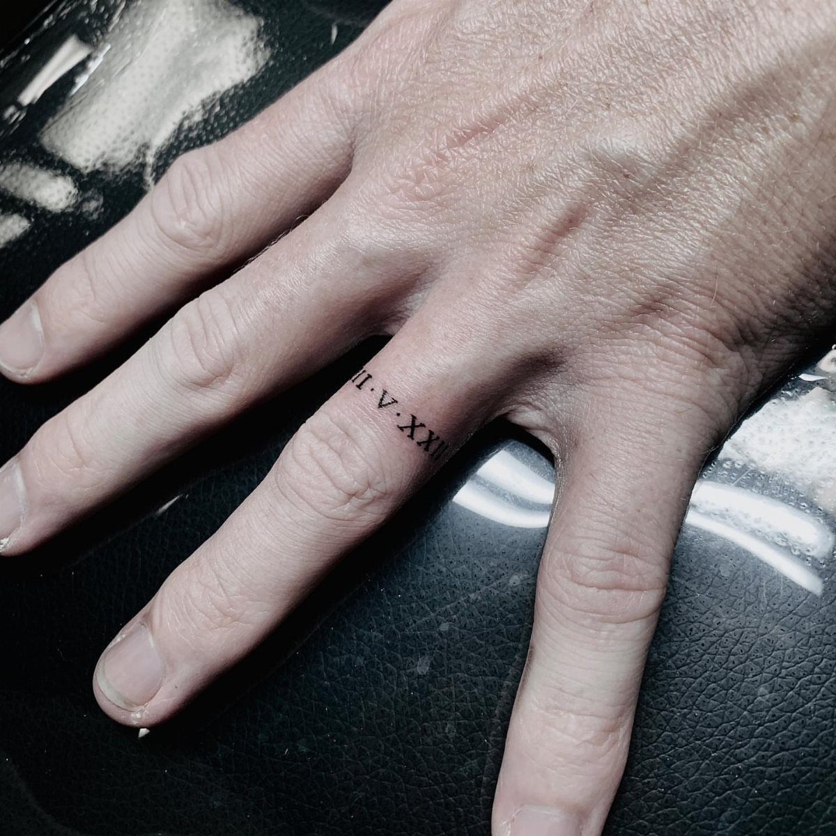 Roman numeral tattoo wrapped around a ring finger like a wedding band