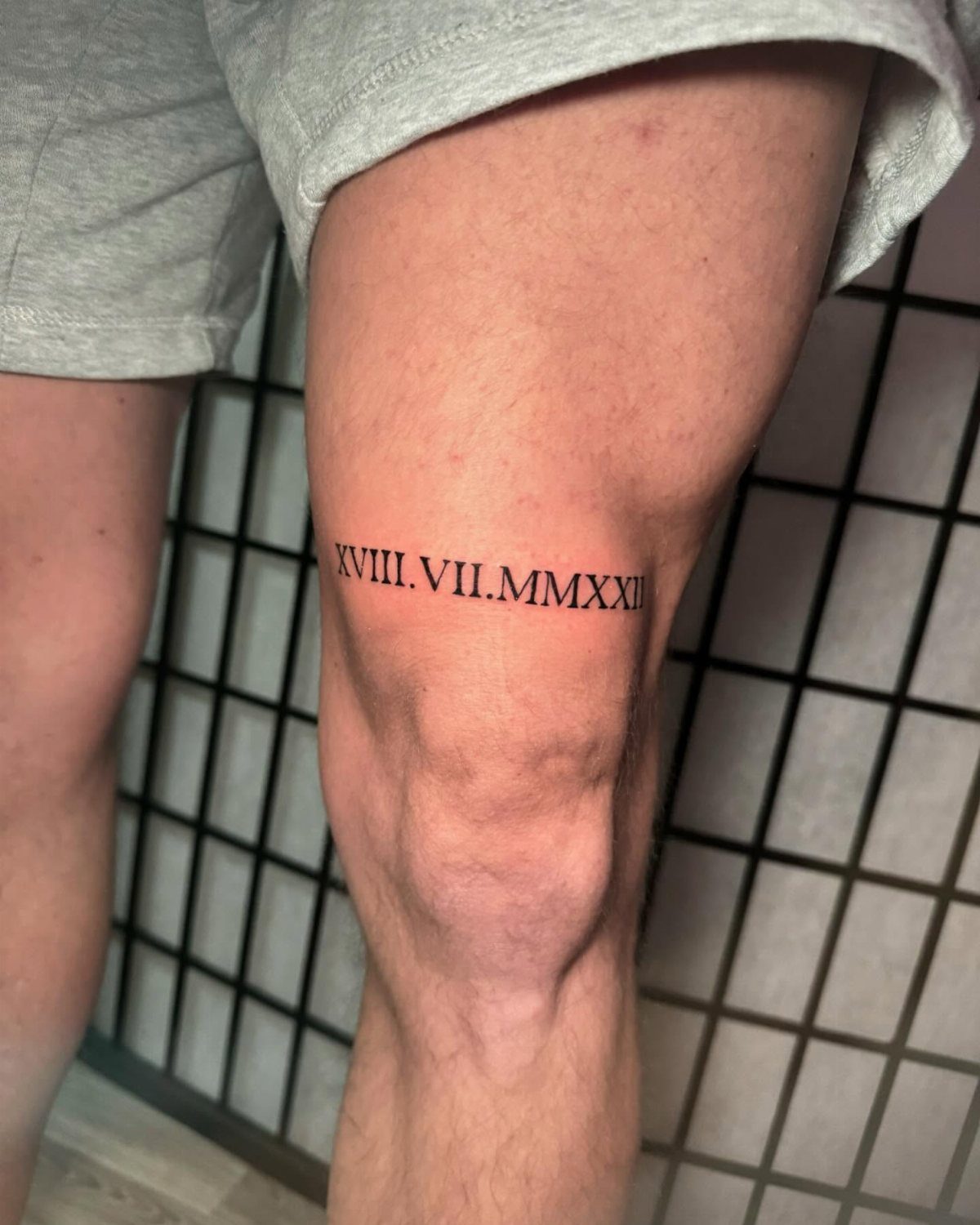 Roman numeral tattoo wrapped around a person's lower thigh above the knee
