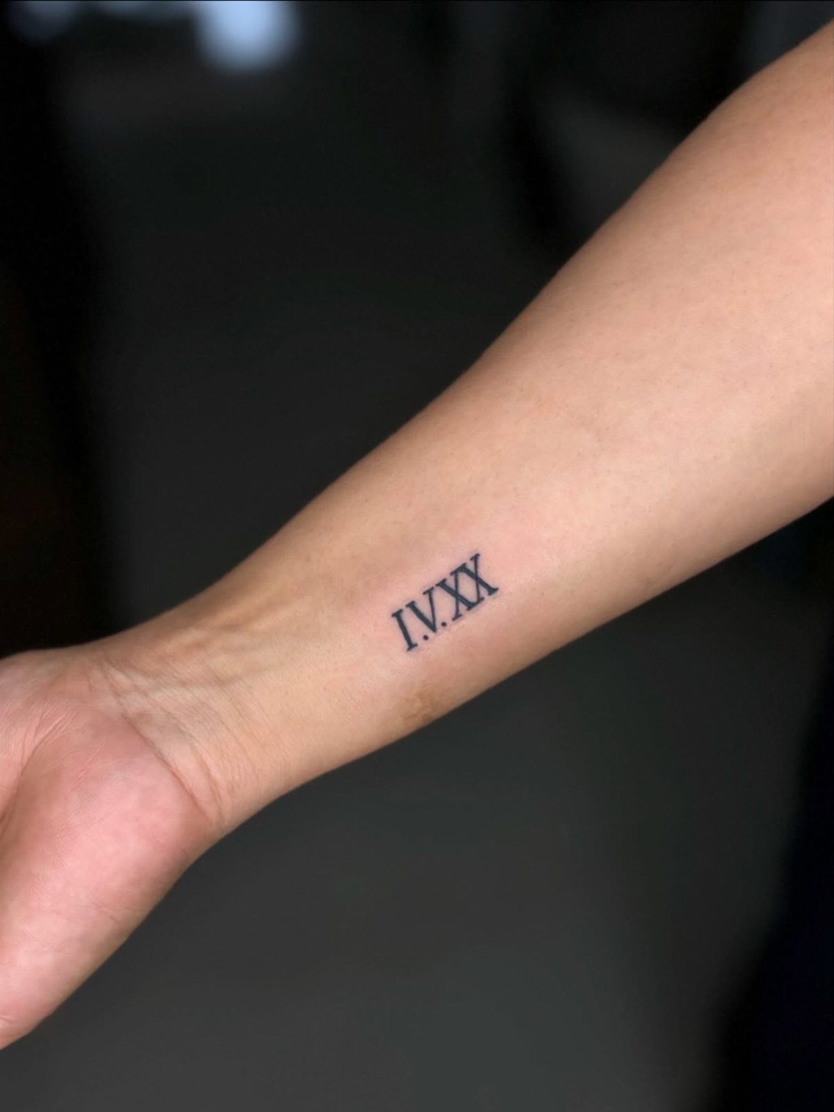 Small black Roman numeral tattoo on the inner wrist of a person.