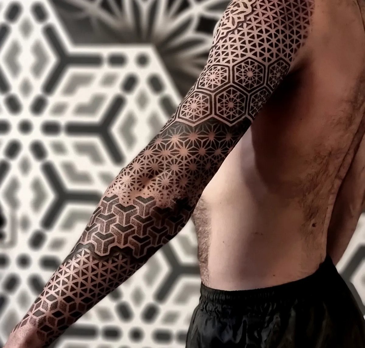 Man's arm with an intricate black ink sacred geometry tattoo of hexagonal patterns.