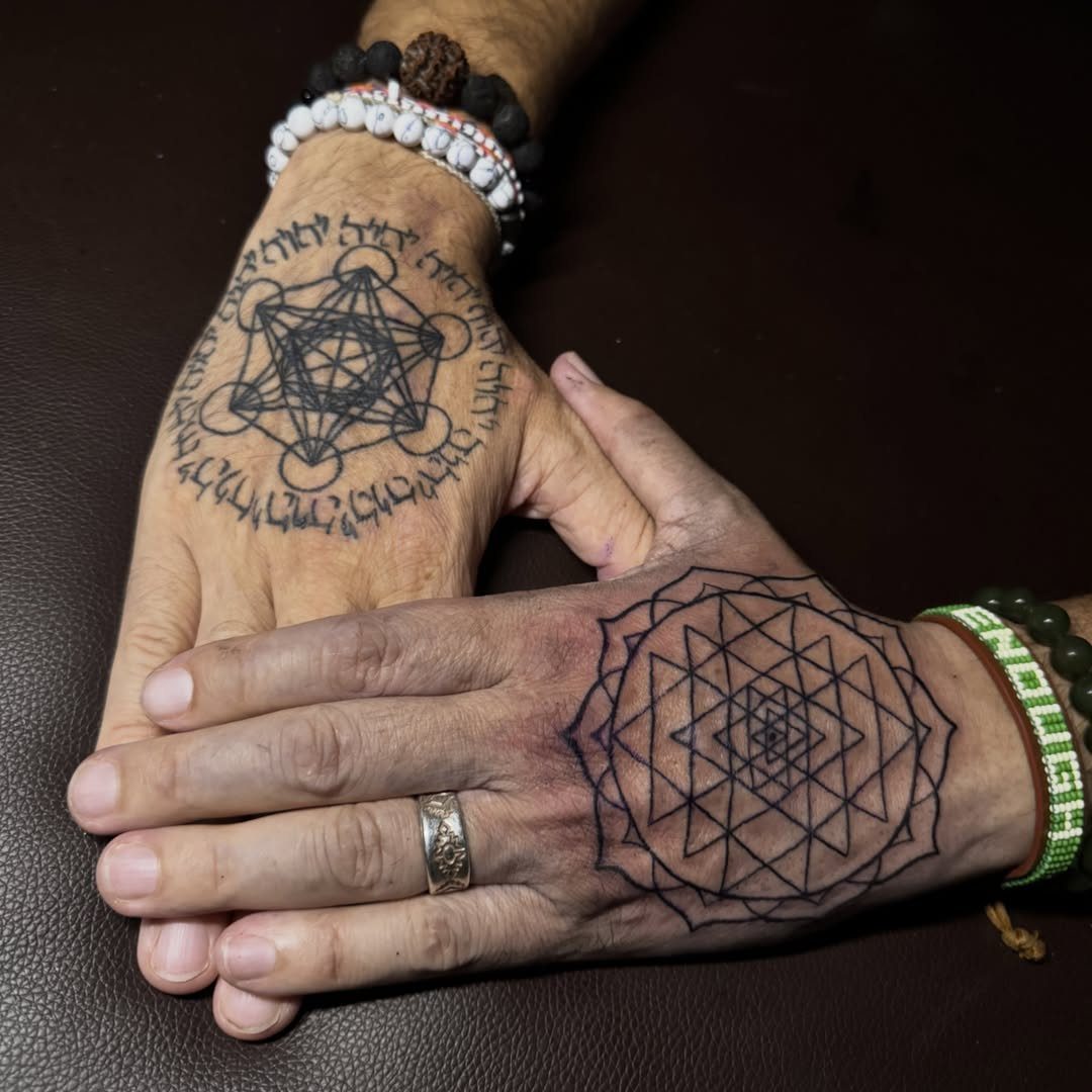 Two hands with intricate black sacred geometry tattoos on the back of palms.