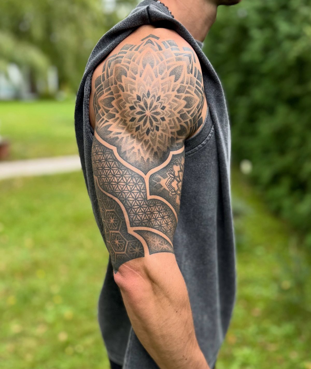 Intricate black ink mandala and geometric tattoo on a person's shoulder and arm.