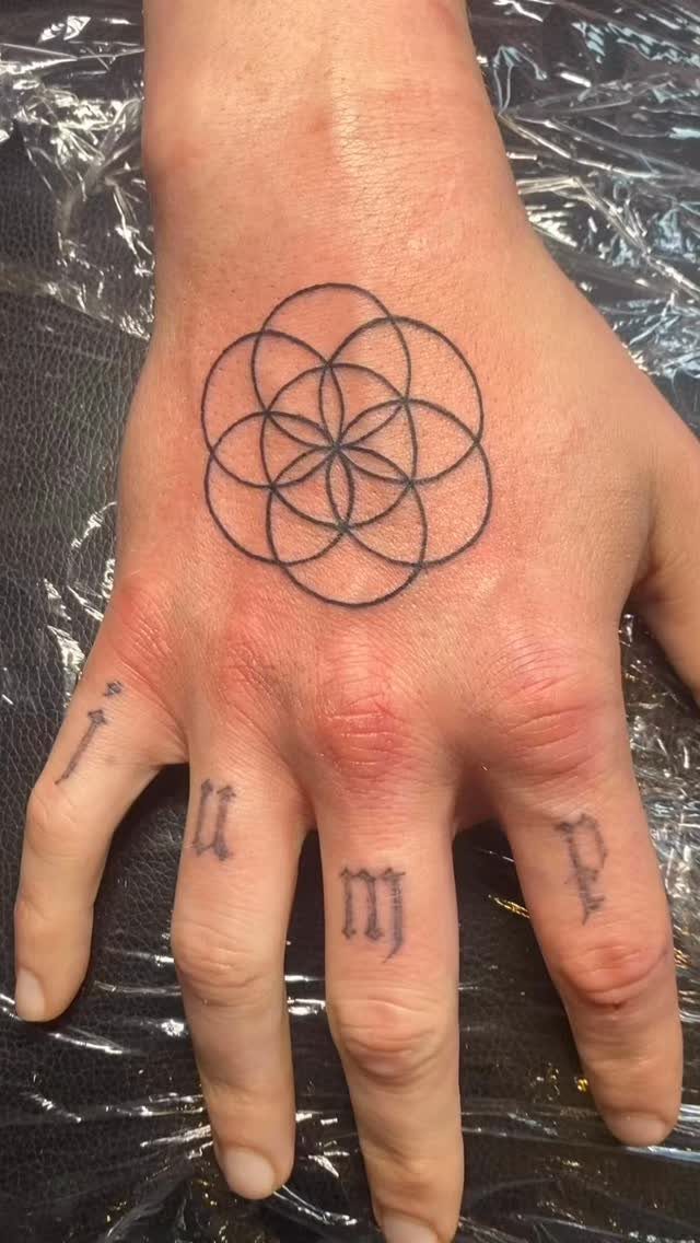 Seed of Life tattoo on the back of a hand with knuckle tattoos.