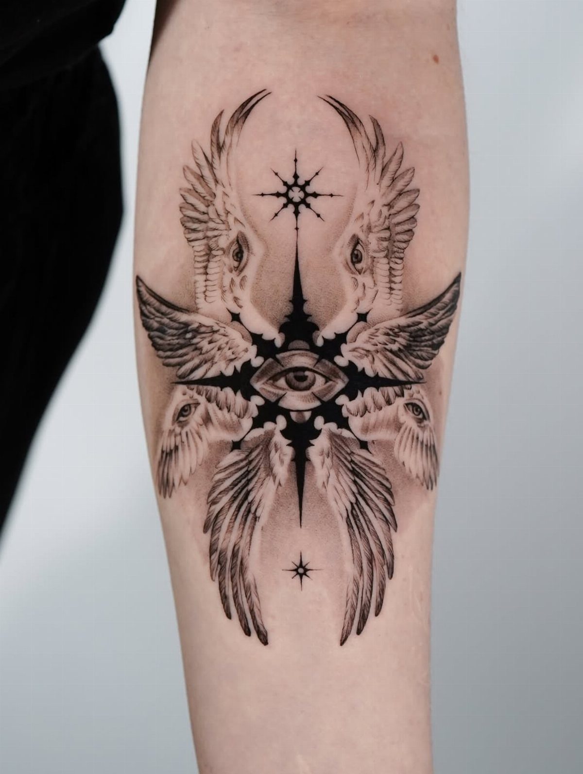 Symmetrical black ink tattoo of birds and an eye on a forearm.