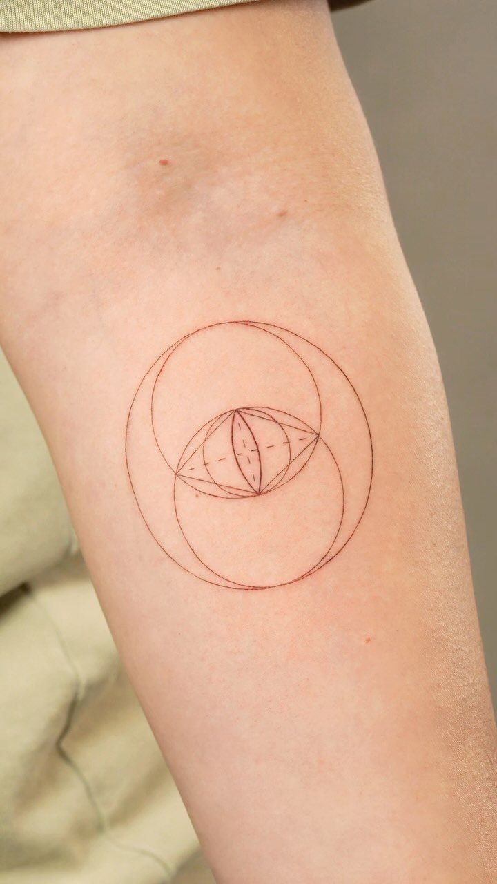 Red ink vesica piscis tattoo on a person's forearm with geometric details.