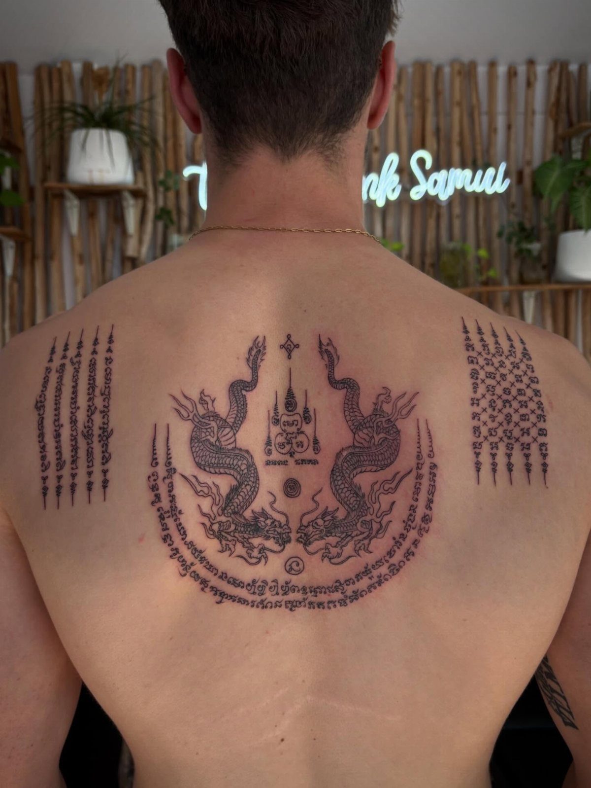 Man's back with traditional Sak Yant tattoos featuring two mythical serpents and geometric patterns.