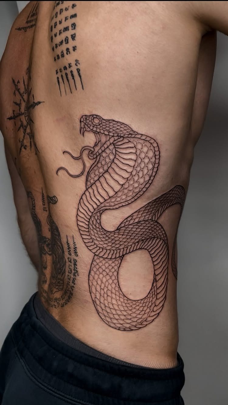 Detailed black ink cobra and traditional Thai script tattoos on a man's torso
