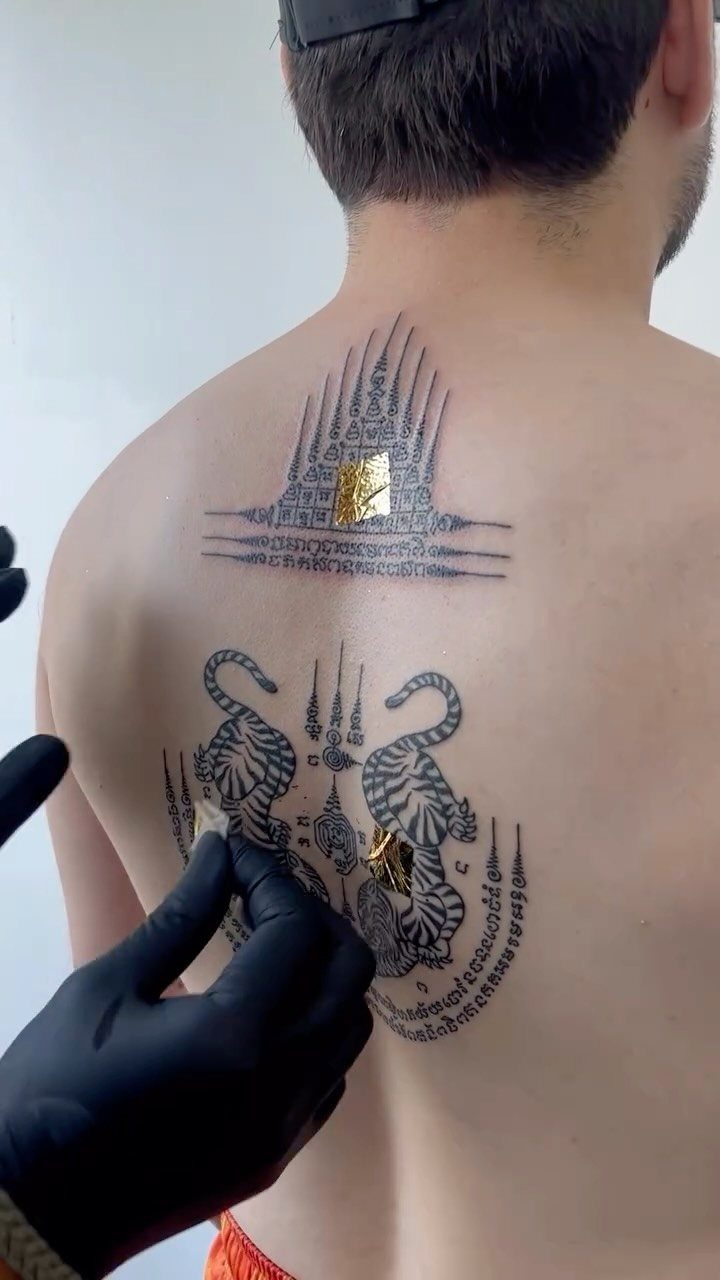 Sak yant tattoos on a man's back with gold leaf being applied.