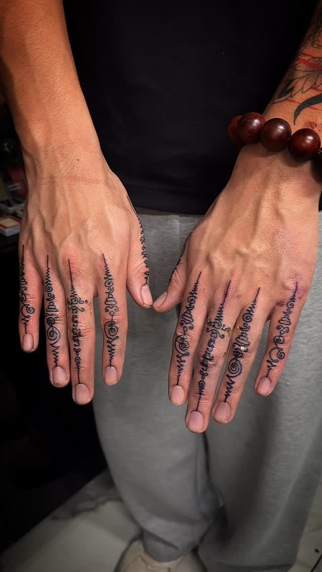 Hands and fingers with intricate black ink Sak Yant tattoos and beaded bracelet.