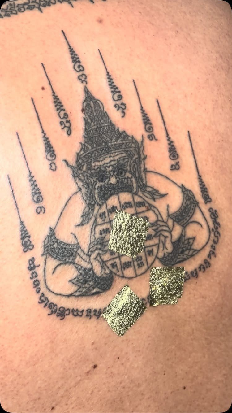 Sak Yant tattoo of Phra Rahu on skin with gold leaf accents