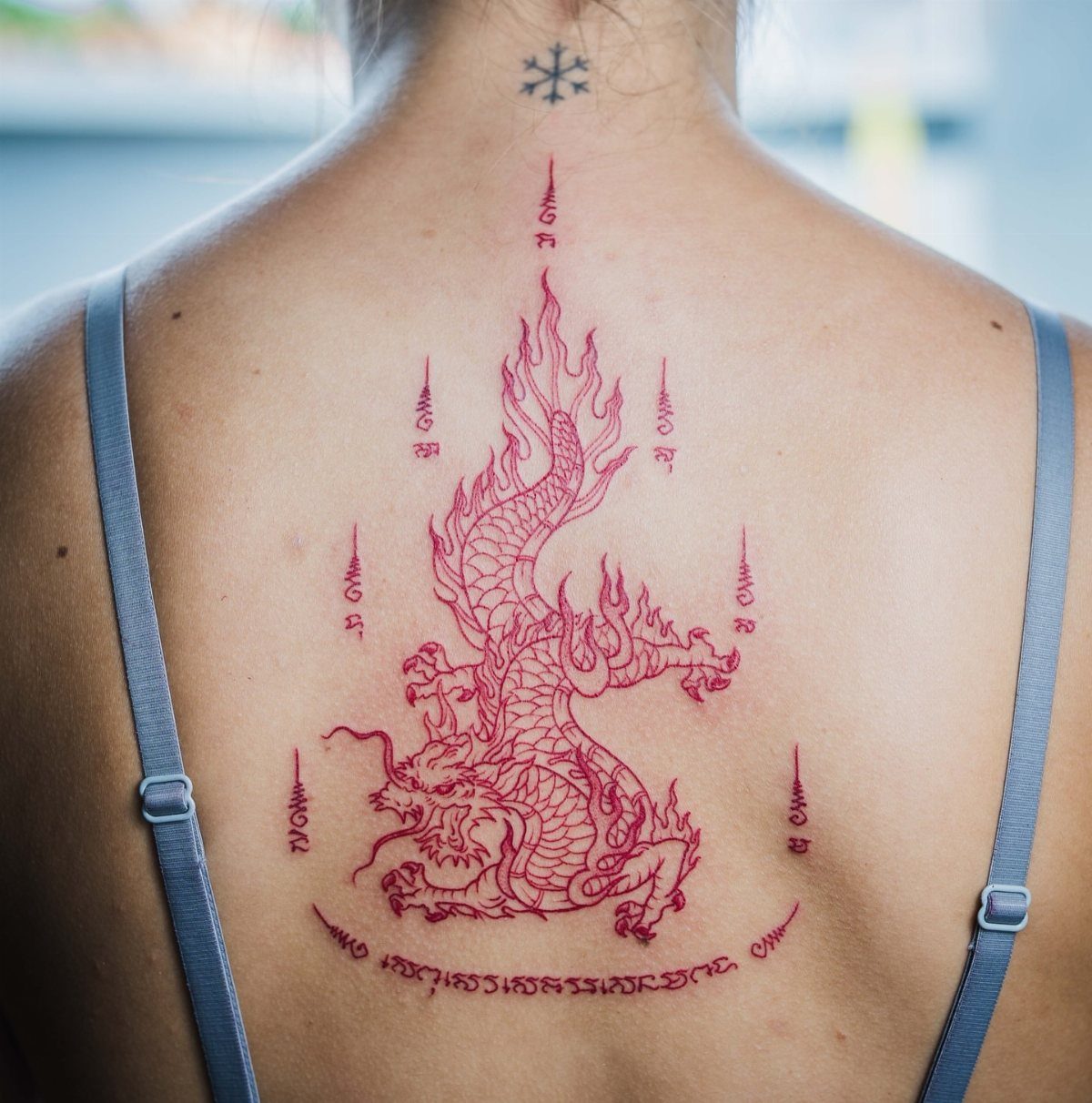 Intricate red Sak Yant tattoo of a mythical creature on a person's back