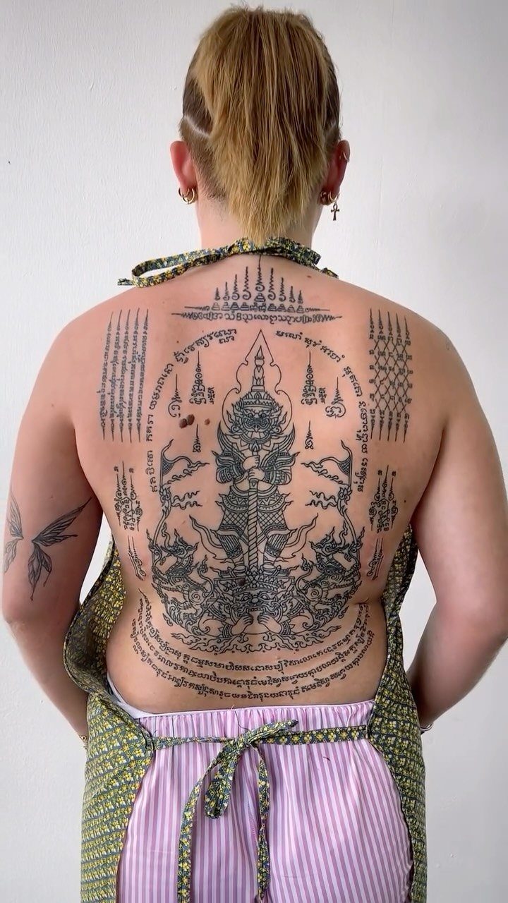 Woman's back featuring a large, detailed black ink Sak Yant tattoo with traditional symbols.