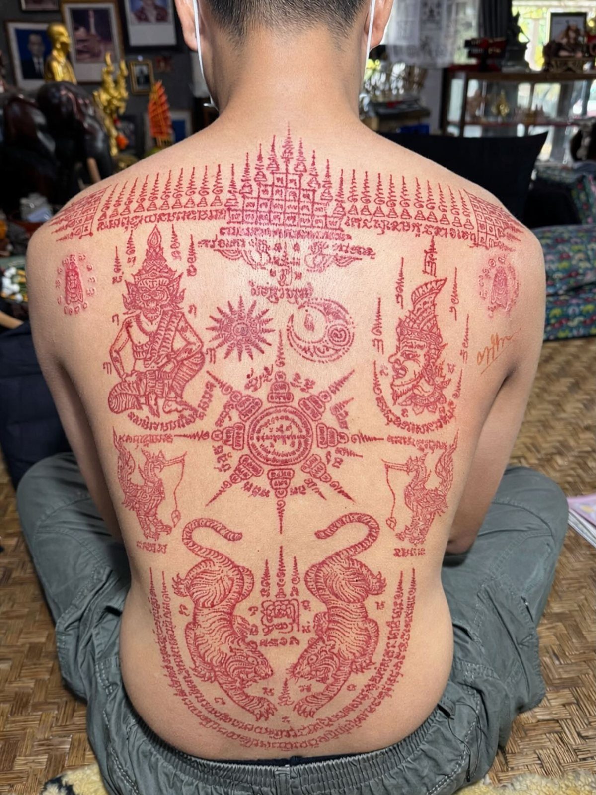 Man's back covered in red Sak Yant tattoos featuring twin tigers and deities.