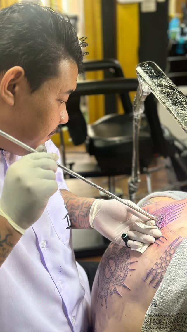Tattoo artist using a traditional long needle to ink a Sak Yant design.