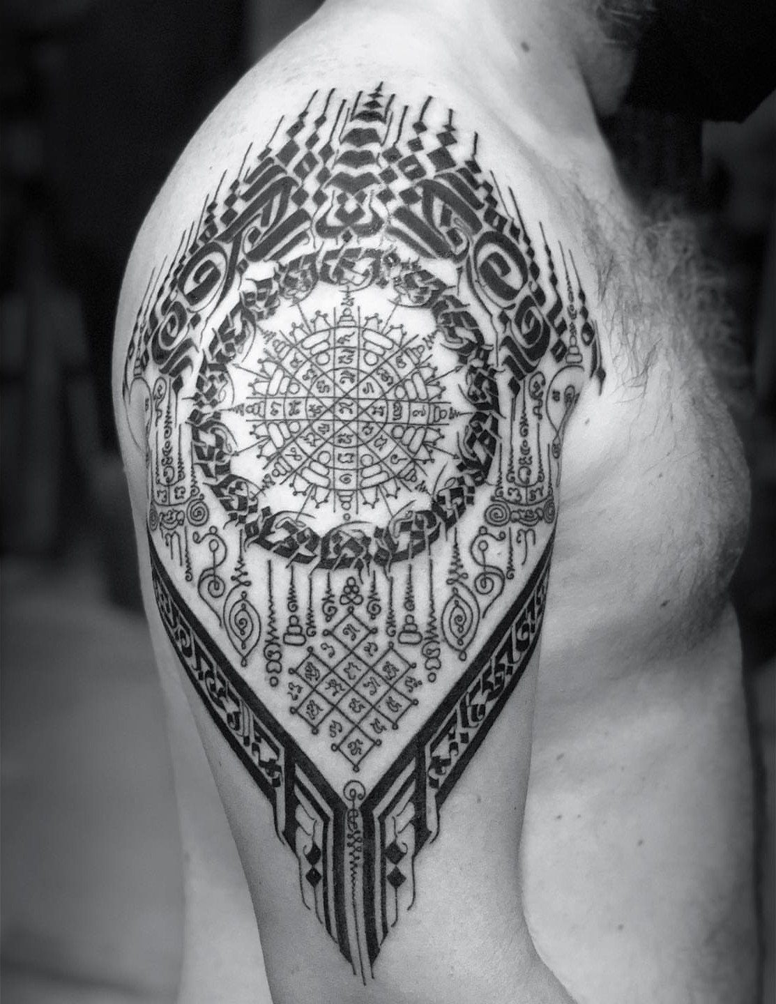 Intricate geometric Sak Yant tattoo on a person's shoulder and upper arm.