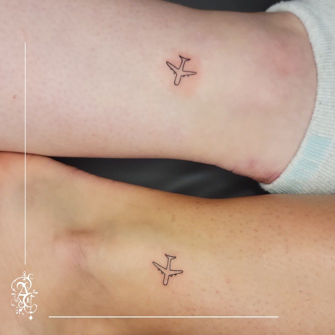 Matching small airplane tattoos on the ankles of two people.