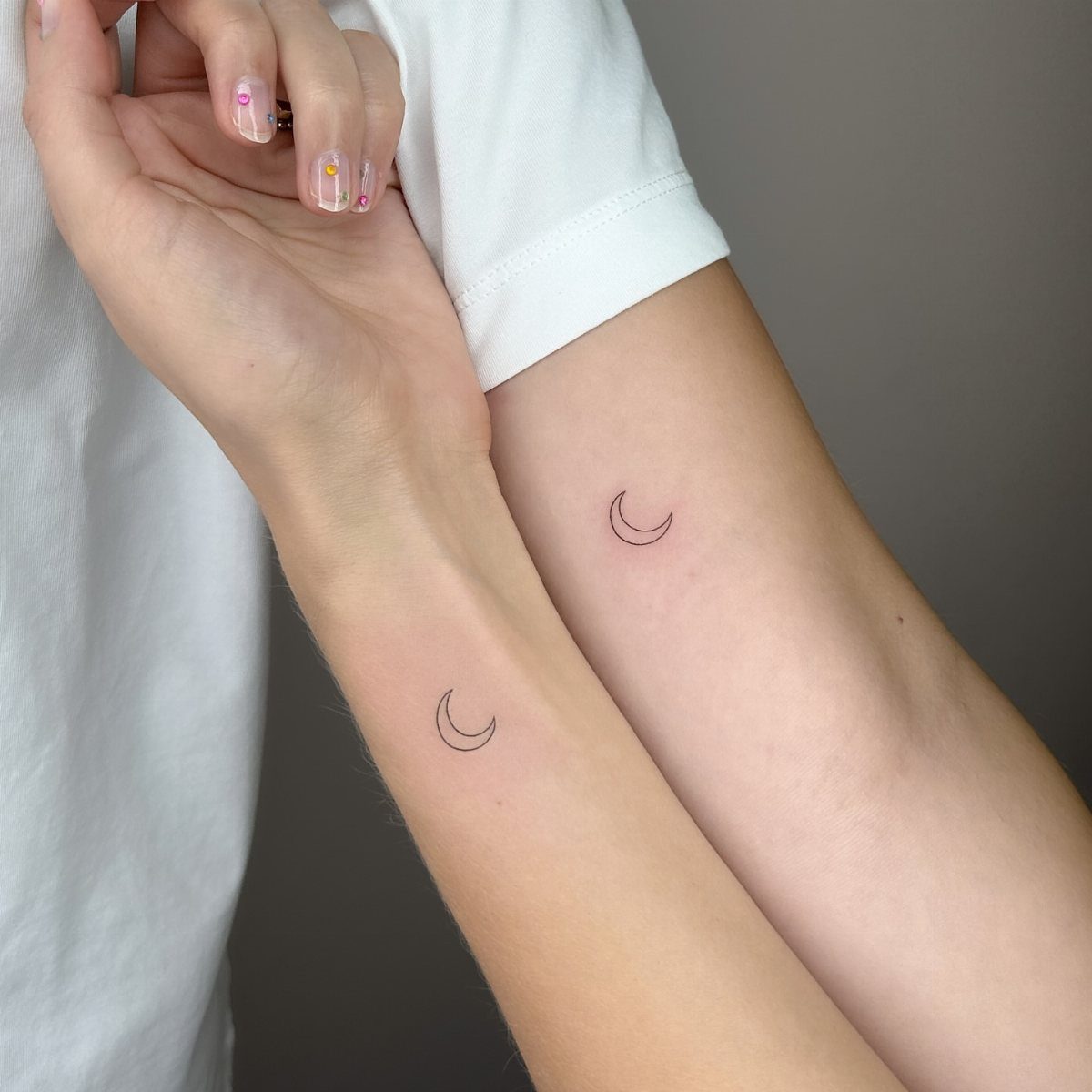 Two forearms with matching small black crescent moon tattoos on the inner wrists.