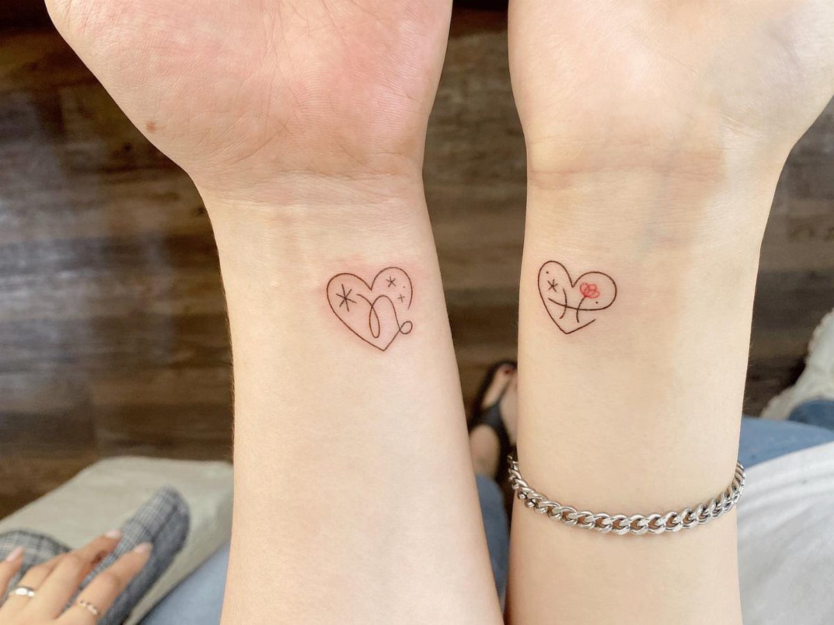 Two wrists with matching small heart tattoos, one with stars and one with a flower.
